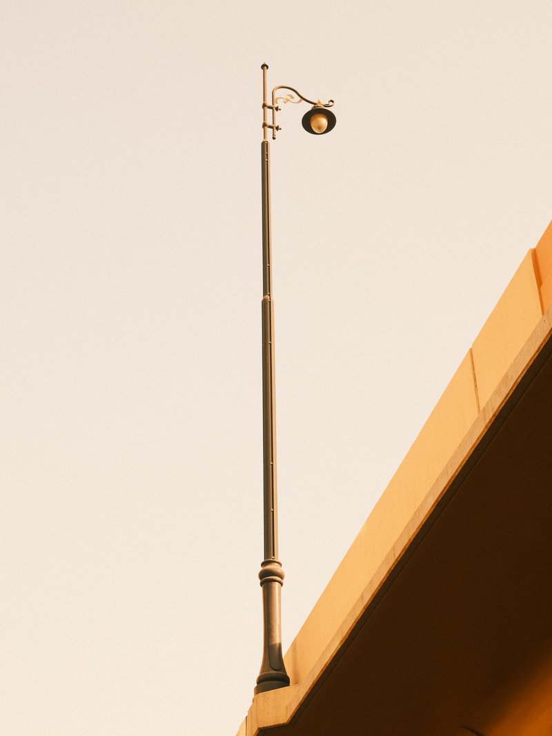 A tall street lamp mounted on a concrete structure against a pale sky.