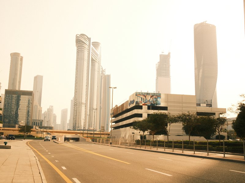 A hazy urban skyline featuring tall skyscrapers under a bright sky with a deserted road in the foreground.