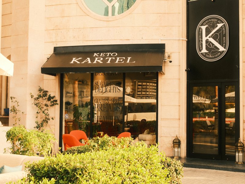 Exterior view of a restaurant named Keto Kartel with outdoor seating and greenery.