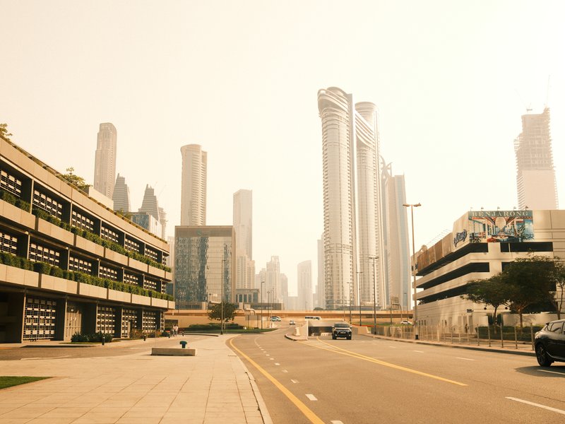 A hazy urban scene featuring tall skyscrapers and a wide street with minimal traffic.