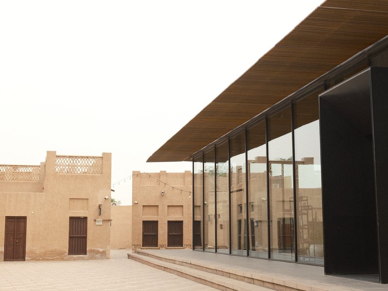 Modern architectural structure with glass facade next to traditional buildings in a desert setting.