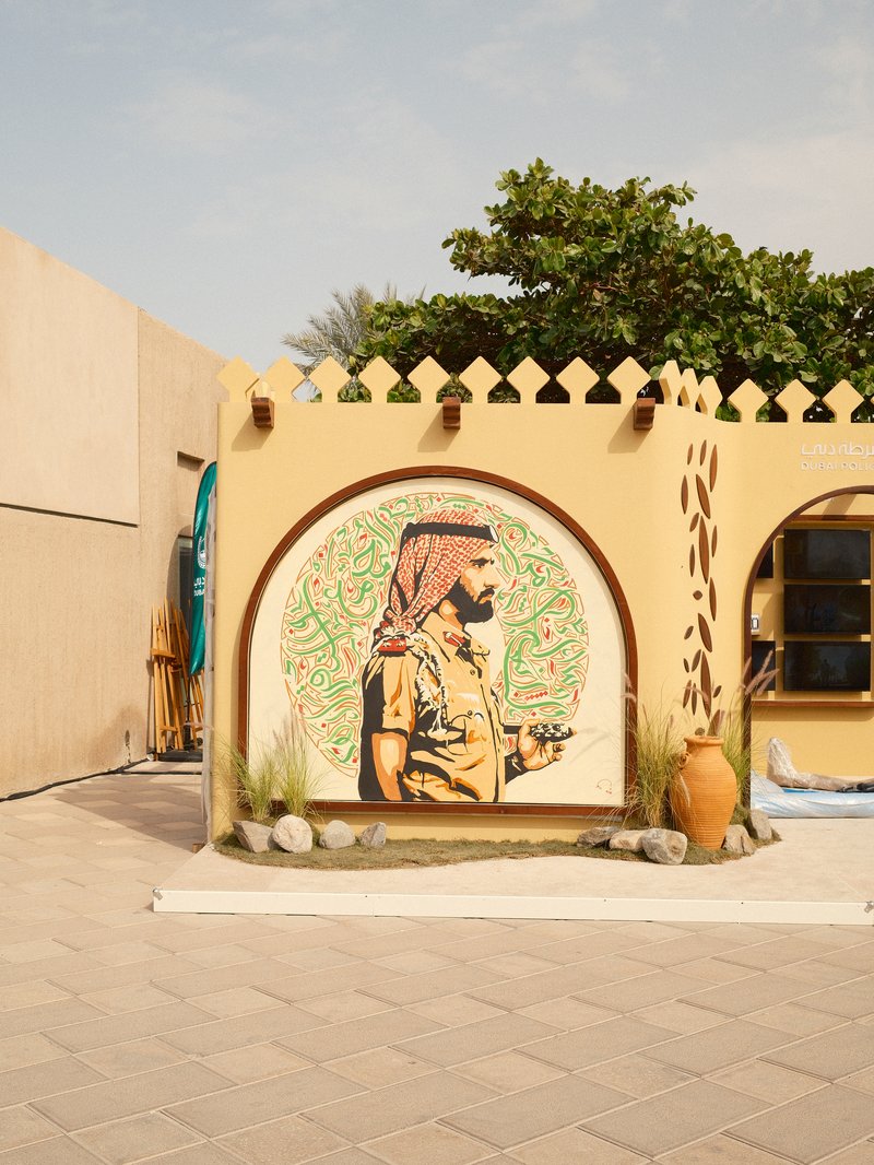 A mural of a man in traditional attire on a yellow wall, surrounded by greenery and decorative elements.
