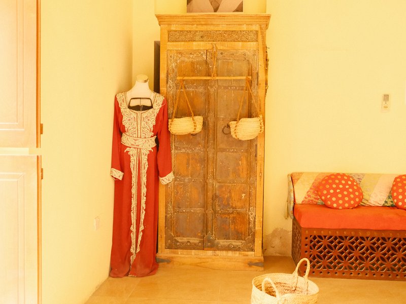 A traditional red dress displayed next to an old wooden door in a bright indoor setting.