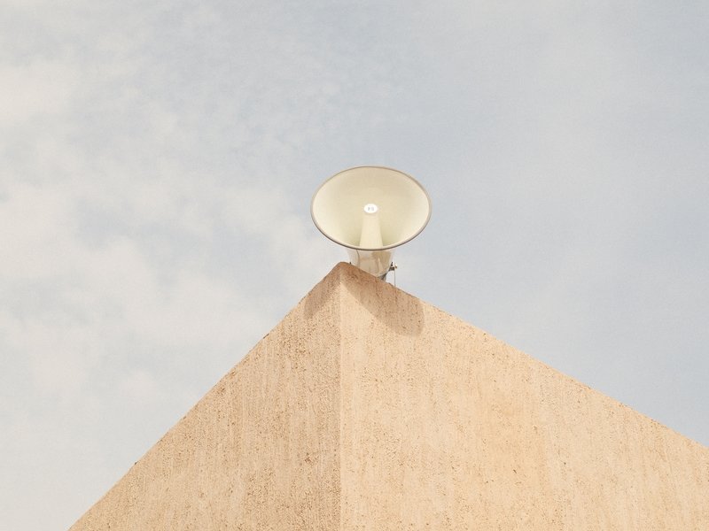 A large speaker mounted on a beige wall under a cloudy sky.