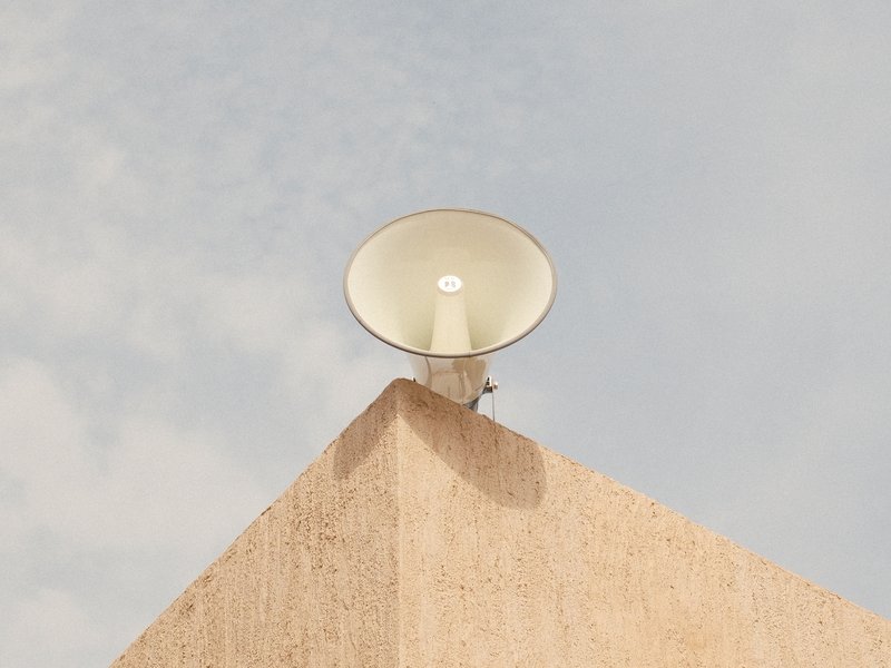 A white megaphone mounted on a beige wall against a cloudy sky.