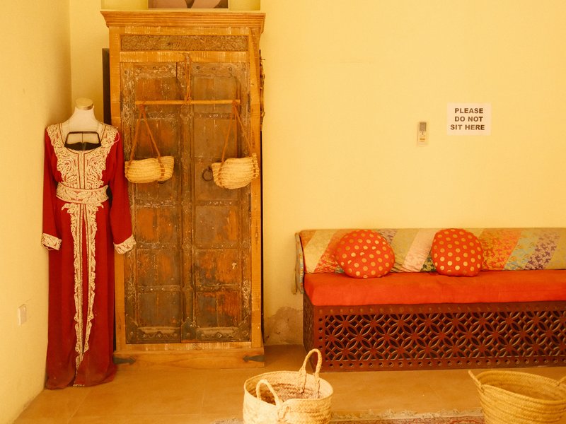 A traditional red dress hangs next to a wooden cabinet in a cozy indoor setting with decorative cushions.