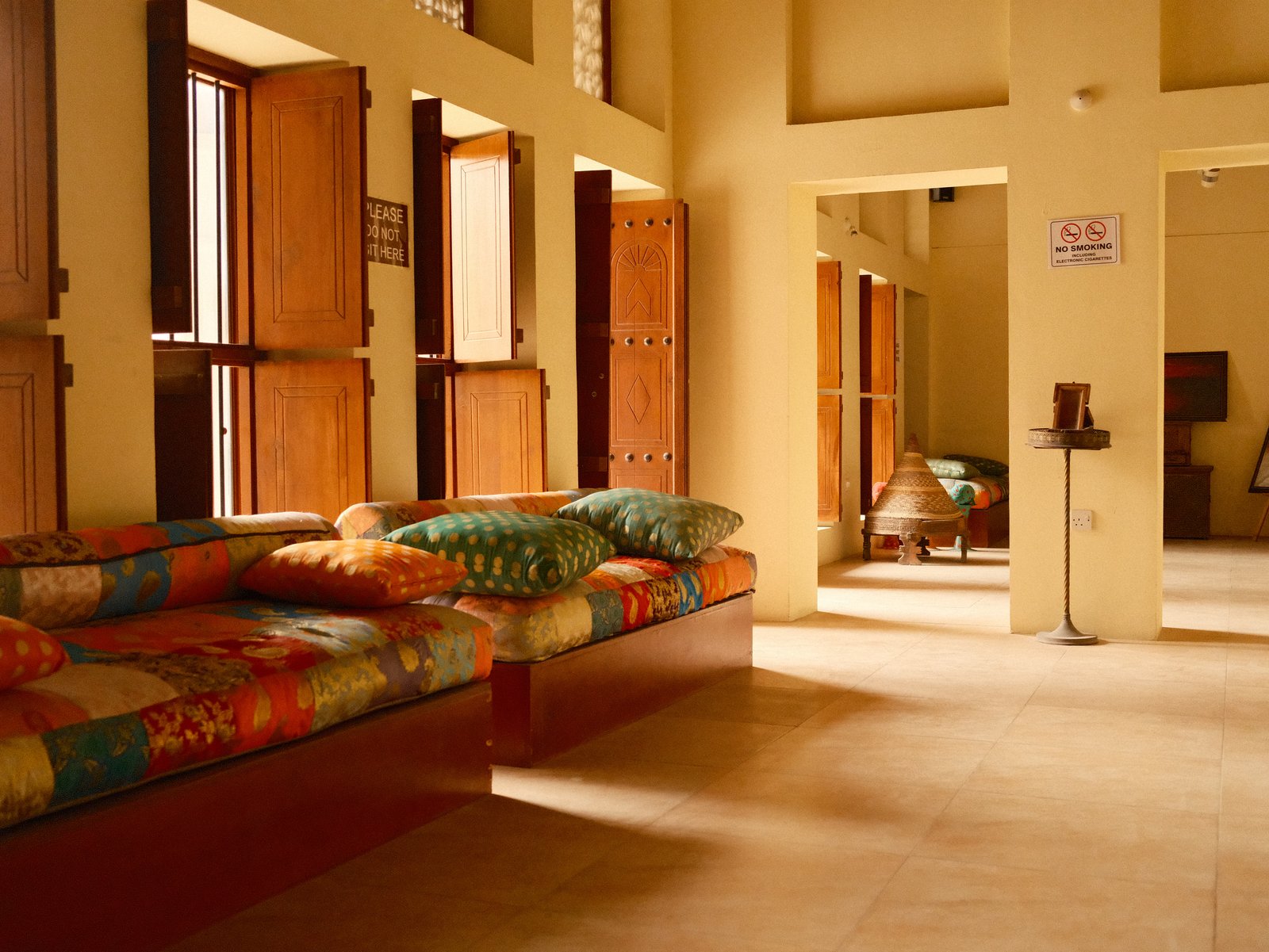 Interior of a cozy room with colorful cushions on a wooden bench and open windows.