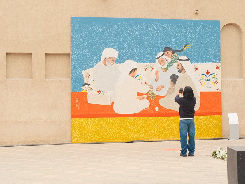 A person photographing a colorful mural depicting people gathered around a table.