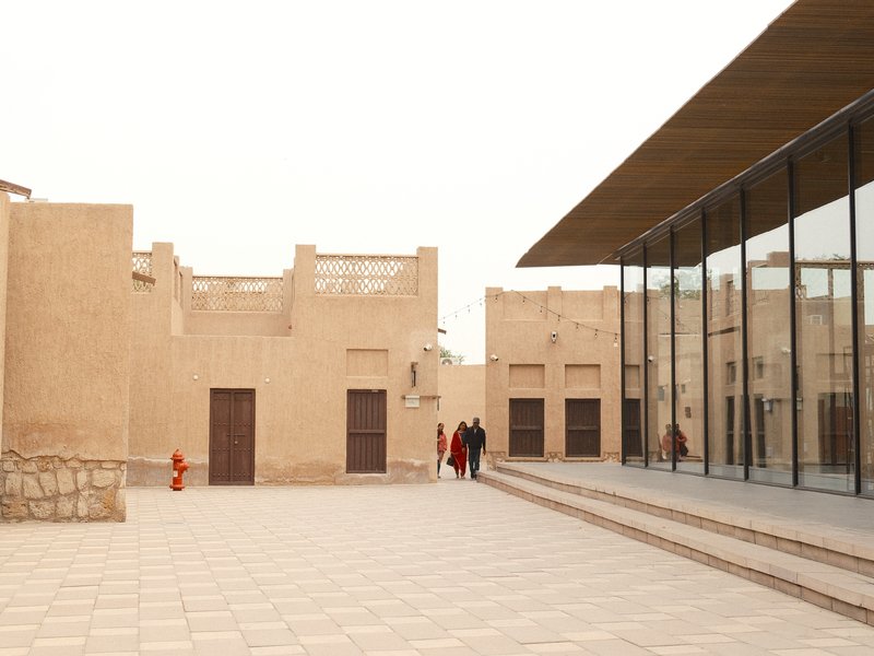 A modern glass building adjacent to traditional mud-brick architecture in a courtyard setting.
