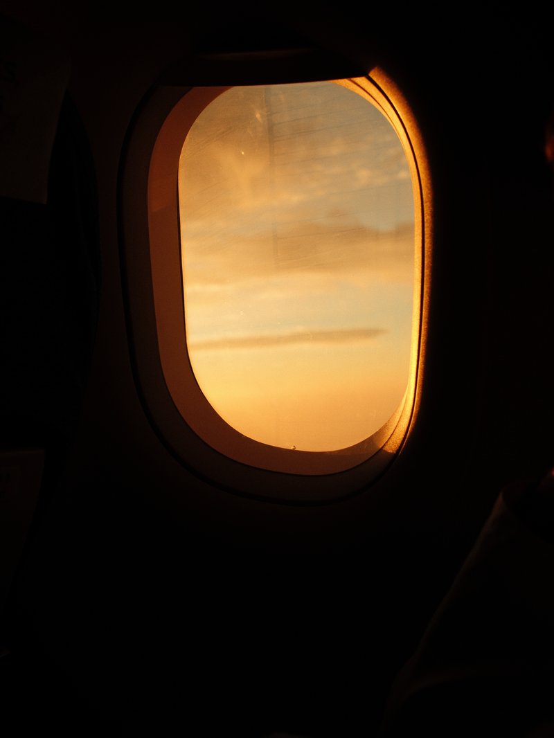 Airplane window view at sunset with warm orange and yellow hues illuminating the sky.