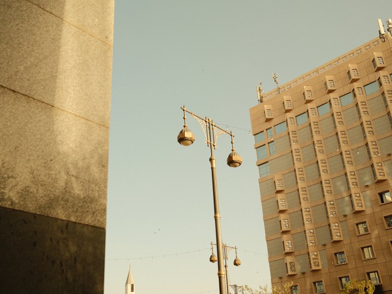 A street scene featuring a tall building and decorative street lamps against a clear sky.