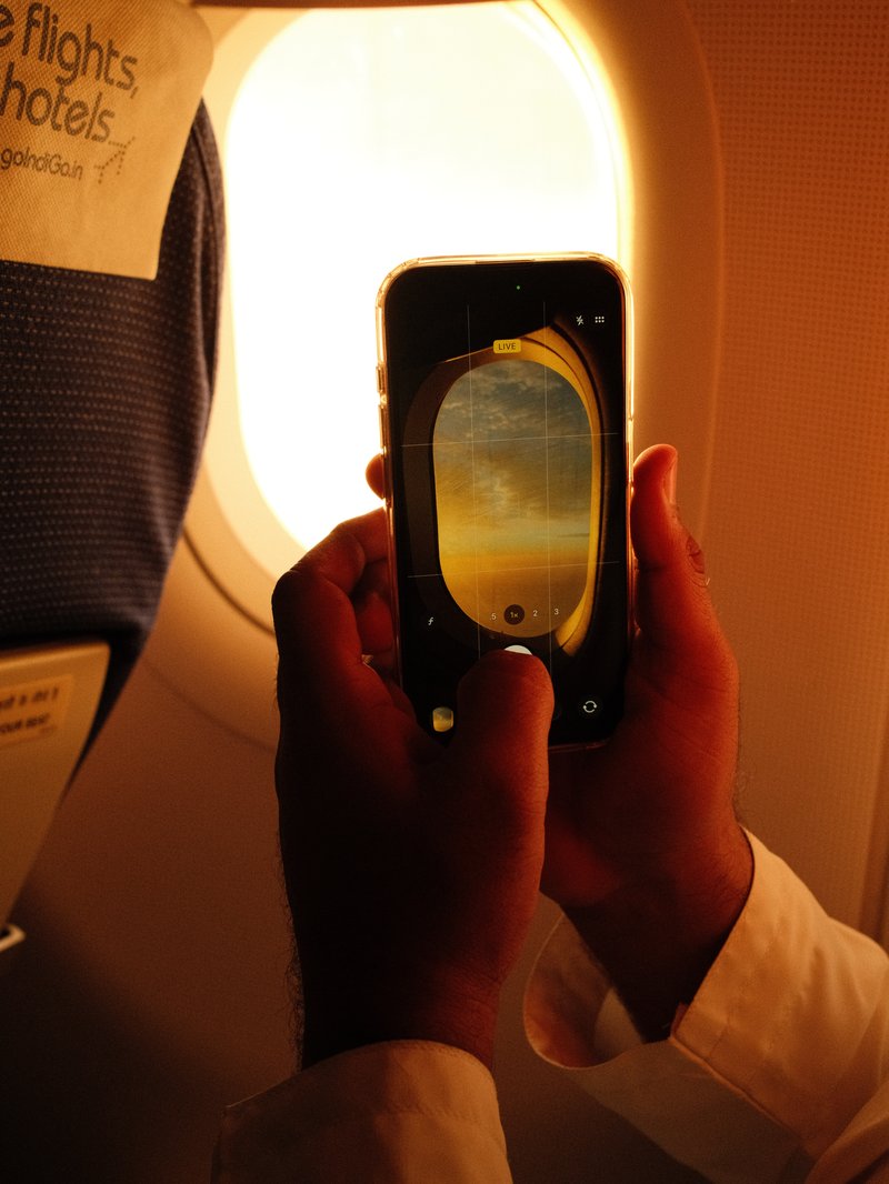 A person holding a smartphone capturing a photo of an airplane window with warm light filtering through.