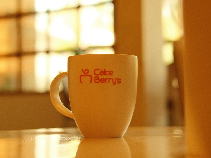 A close-up of a white coffee mug with a logo on a table, soft light filtering through a window.