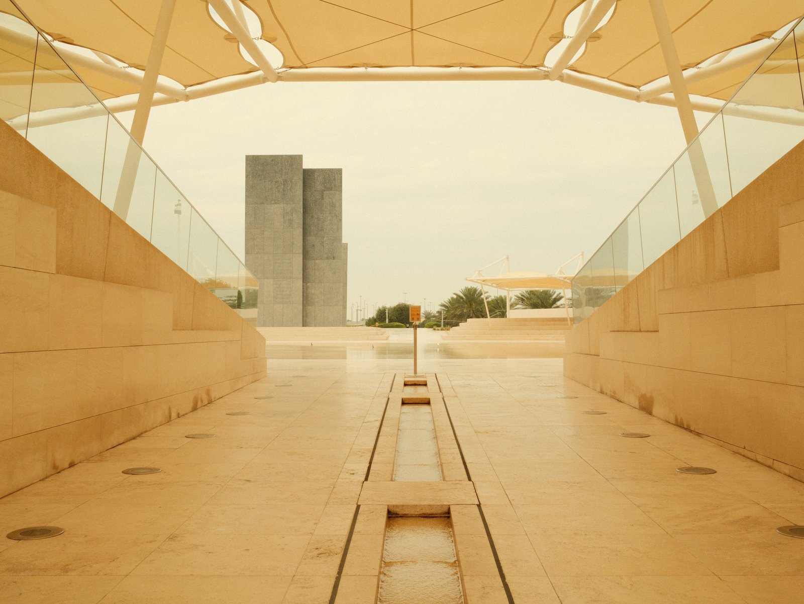 View of a modern architectural structure with a pathway leading towards tall buildings in the background.