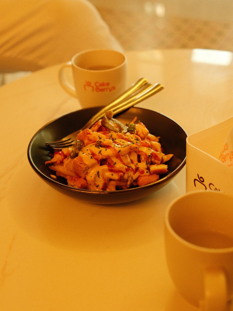 A close-up of a black bowl filled with colorful food, two cups of coffee on a table.