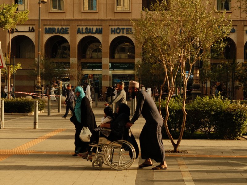 A group of people walking in an urban setting, with one person in a wheelchair being assisted.