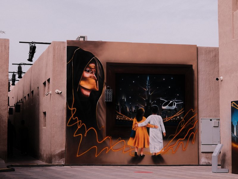 A colorful mural depicting two children walking towards a starry night, with a large face in the background.