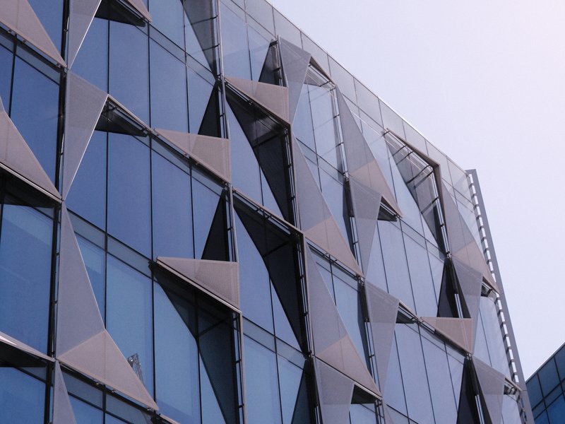 Close-up of a modern building facade with geometric glass panels reflecting the sky.