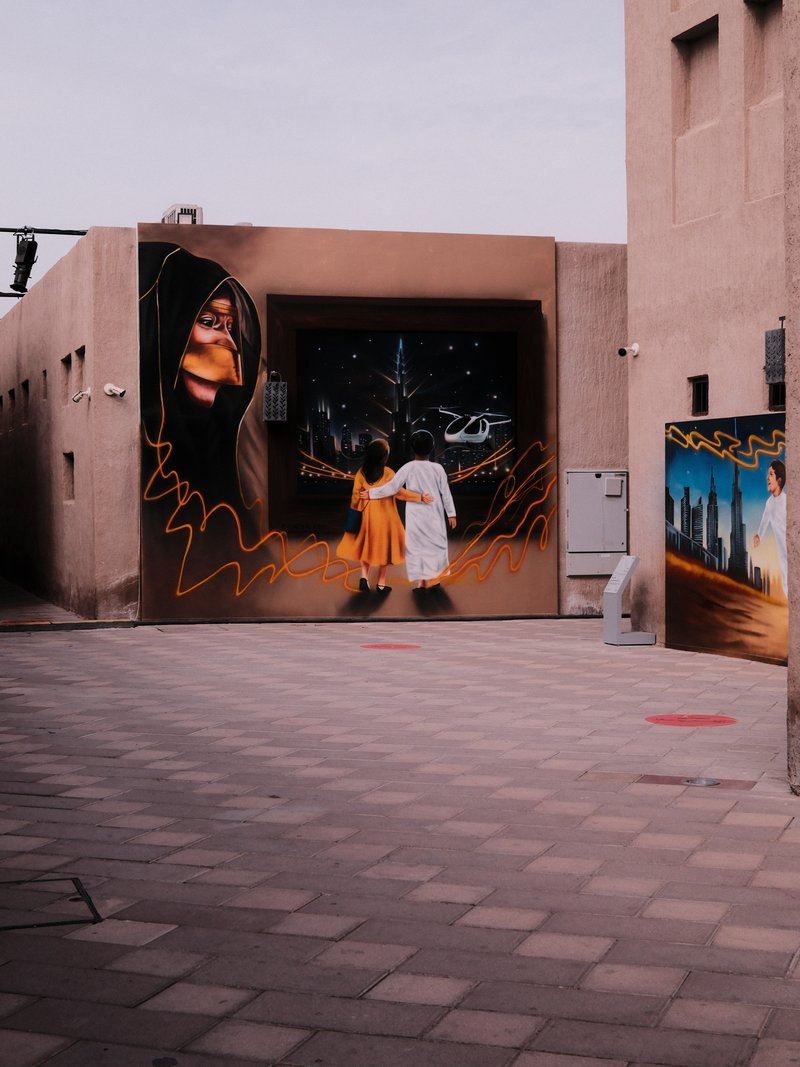 A narrow alley with colorful murals on the walls, showcasing a woman and a man in traditional attire.