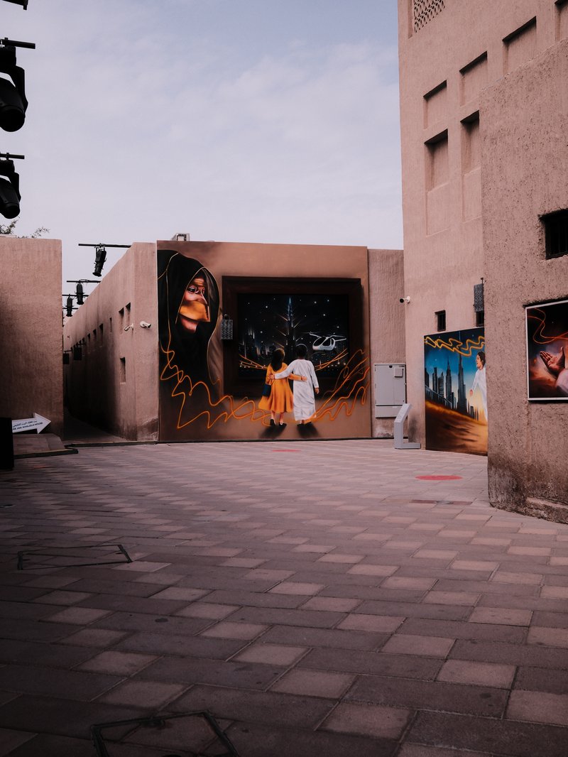 Two people walking in an urban alley with graffiti on the walls and a cloudy sky above.