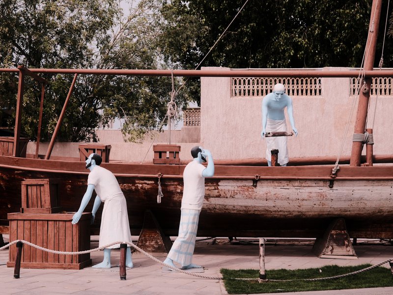 Three figures in traditional attire interacting with a wooden boat in a historical setting.