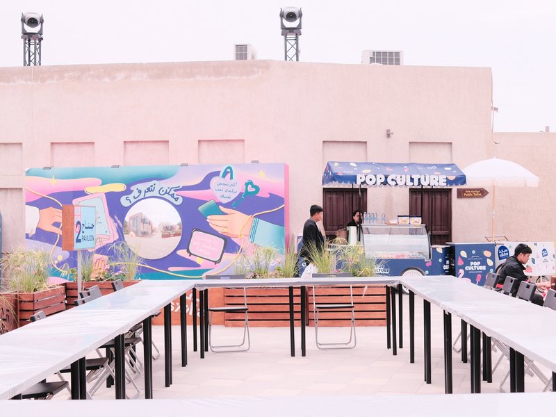 Outdoor café scene with colorful mural and ice cream stand, featuring tables and patrons.