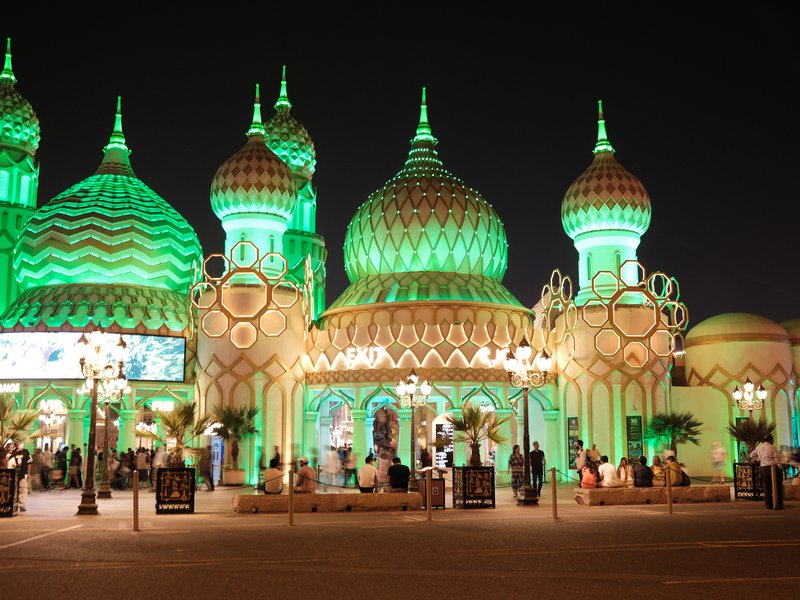 Colorful illuminated architecture with domes and spires at night, surrounded by palm trees.