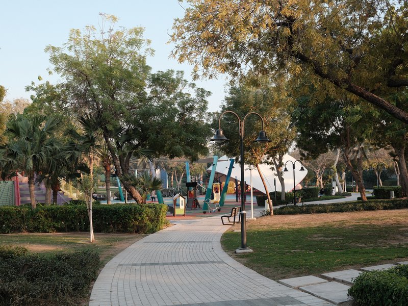 A serene park pathway leading through lush greenery with playground equipment in the background.