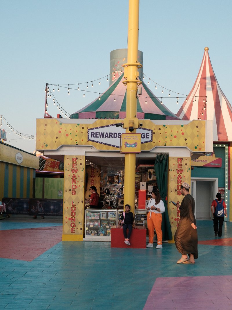 Colorful carnival scene with a rewards booth and people interacting in a festive atmosphere.