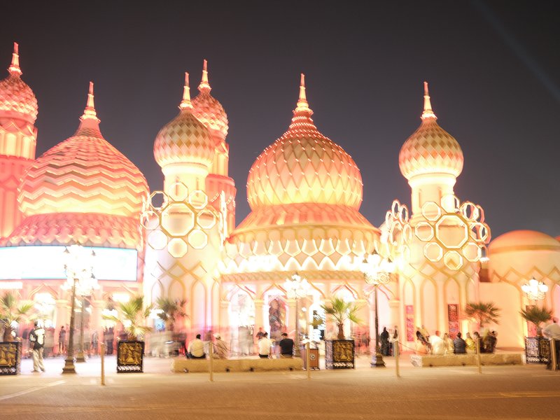 Illuminated architectural structures with ornate domes and vibrant lighting at night.