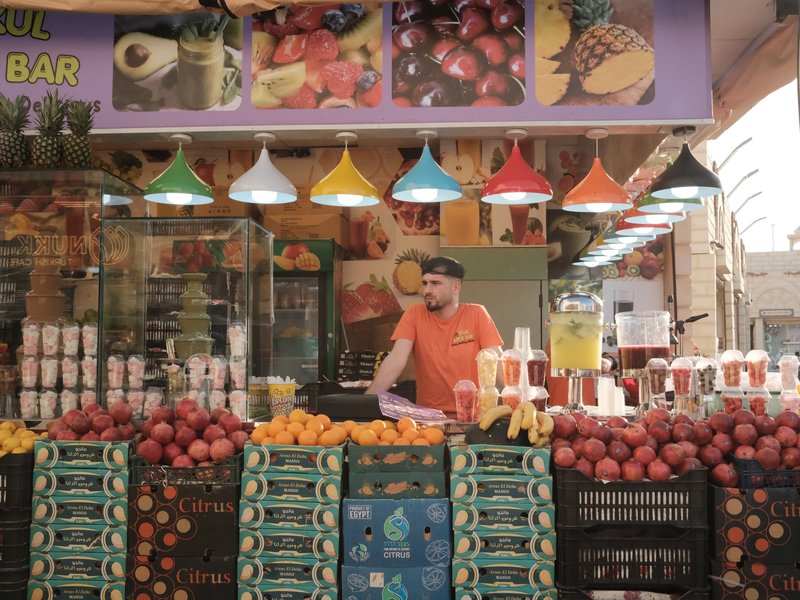 A vibrant fruit market stall with colorful hanging lamps and a vendor arranging fruits.