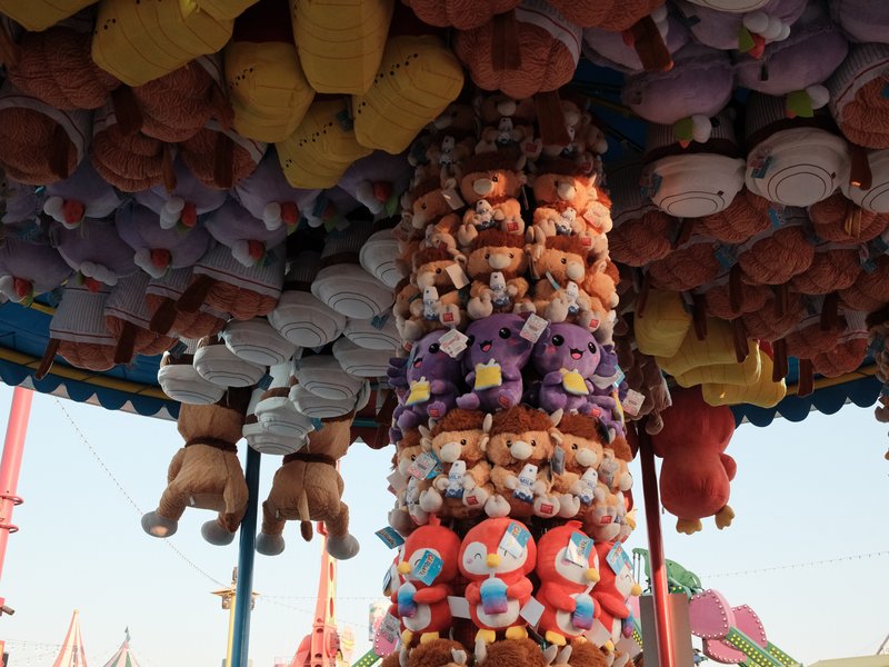Colorful collection of stuffed animals hanging from a carnival ride, under a bright sky.