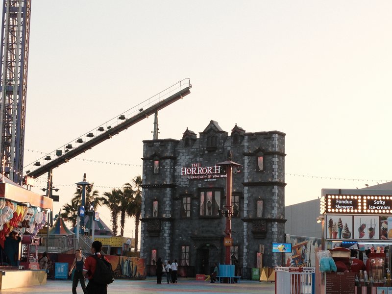 A spooky castle attraction at a fairground during sunset with rides in the background.