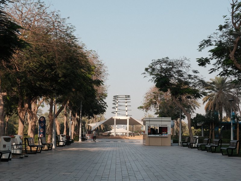A quiet promenade lined with trees and benches, leading to a modern structure in the distance.