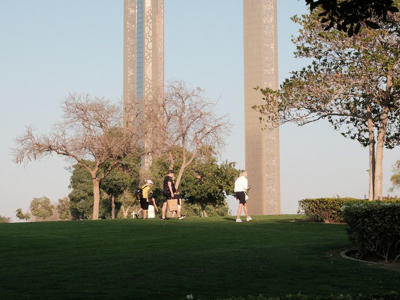 People walking on a green lawn with tall structures in the background during golden hour.