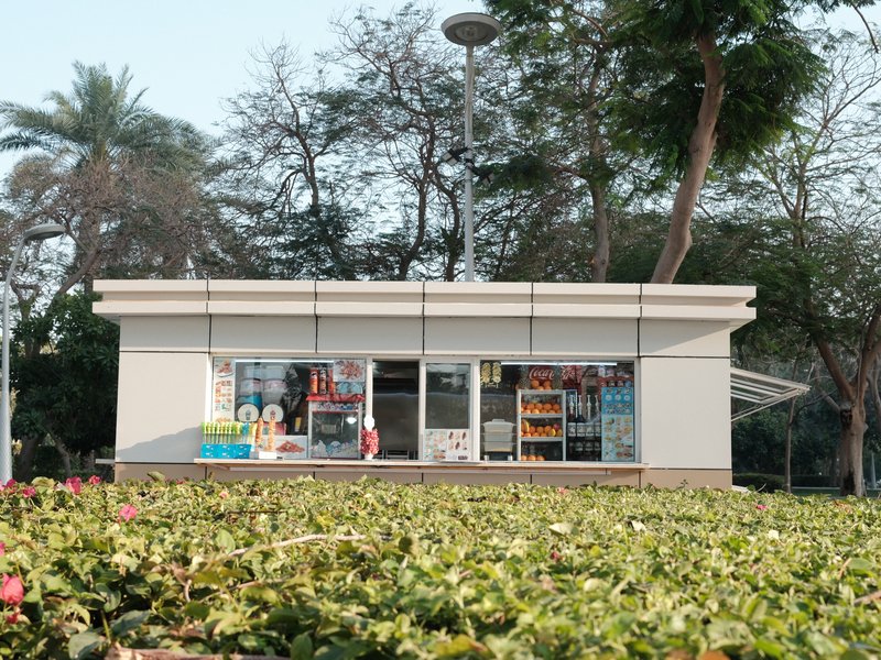 A small shop with large windows surrounded by green bushes and trees in a park setting.