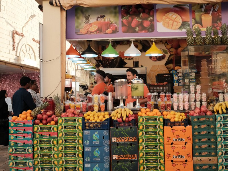 A vibrant fruit stall with colorful displays of fruits and two vendors in orange shirts.
