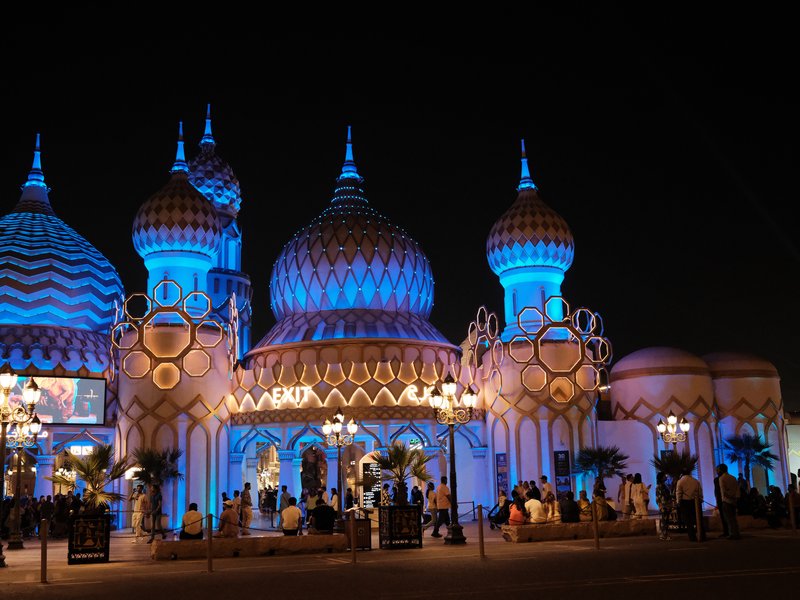 Colorful illuminated architecture with domes and spires at night, surrounded by people.