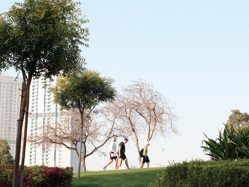 Two people walking on a grassy hill with trees and buildings in the background under a clear sky.