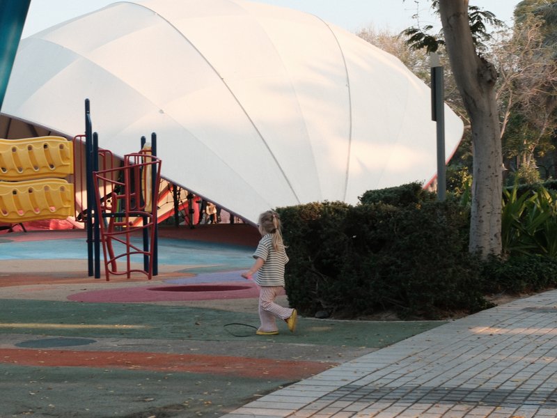 A child walking in a playground with colorful equipment and a large white canopy overhead.