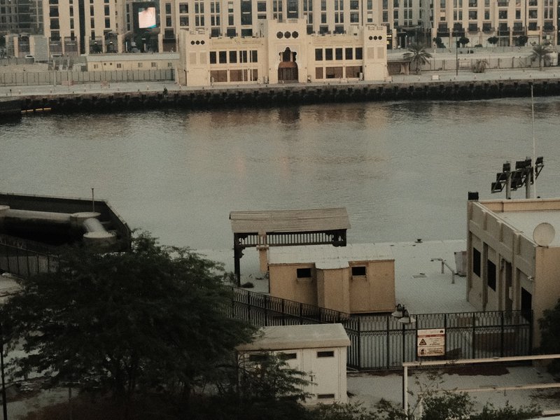 A view of a waterfront with buildings and structures reflected in the water, under a muted sky.