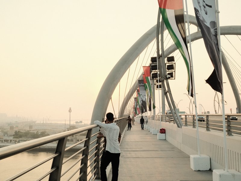 A person leaning on a railing of a modern bridge with flags in the background during sunset.