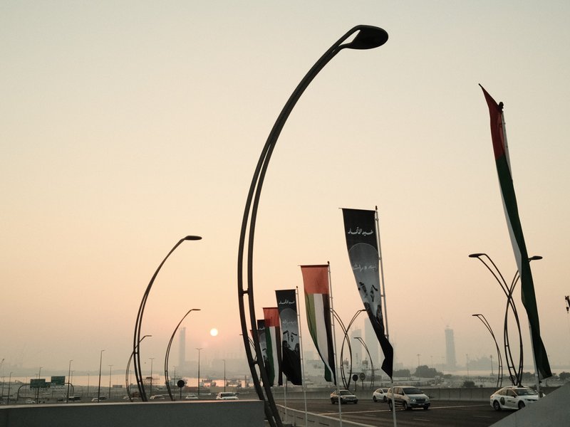 A sunset scene with curved streetlights and flags along a road, creating a serene atmosphere.