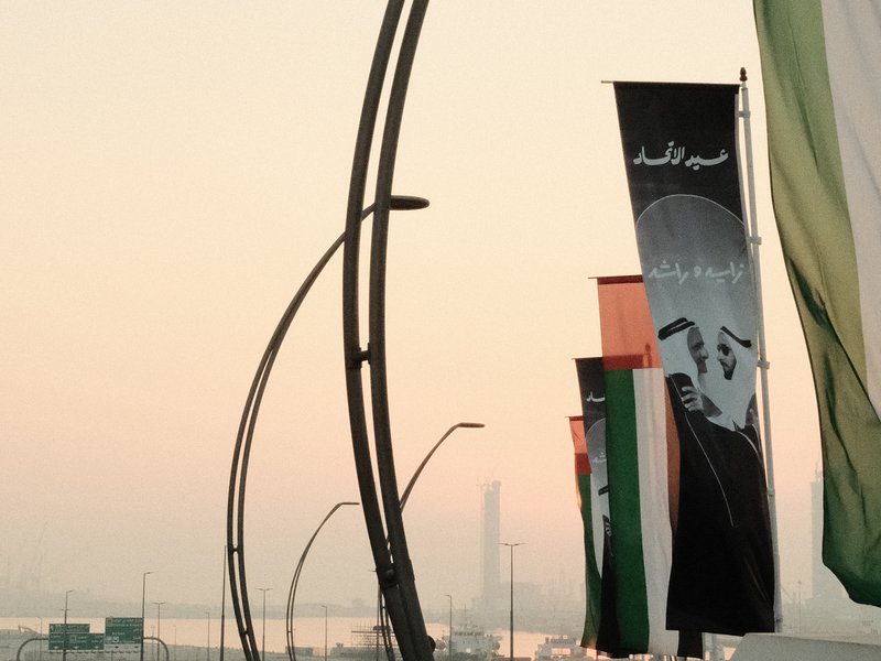 Banners with Arabic text and images against a soft pastel sky, with a city skyline in the background.