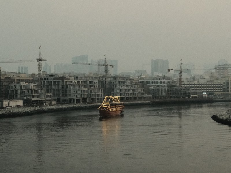 A yellow boat navigating a river surrounded by construction sites and hazy city skyline.