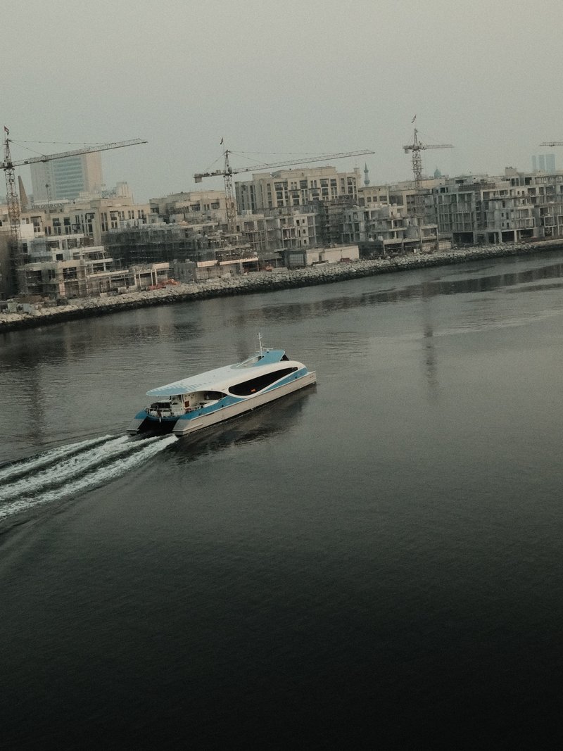 A boat navigating through calm waters near a construction site with cranes in the background.