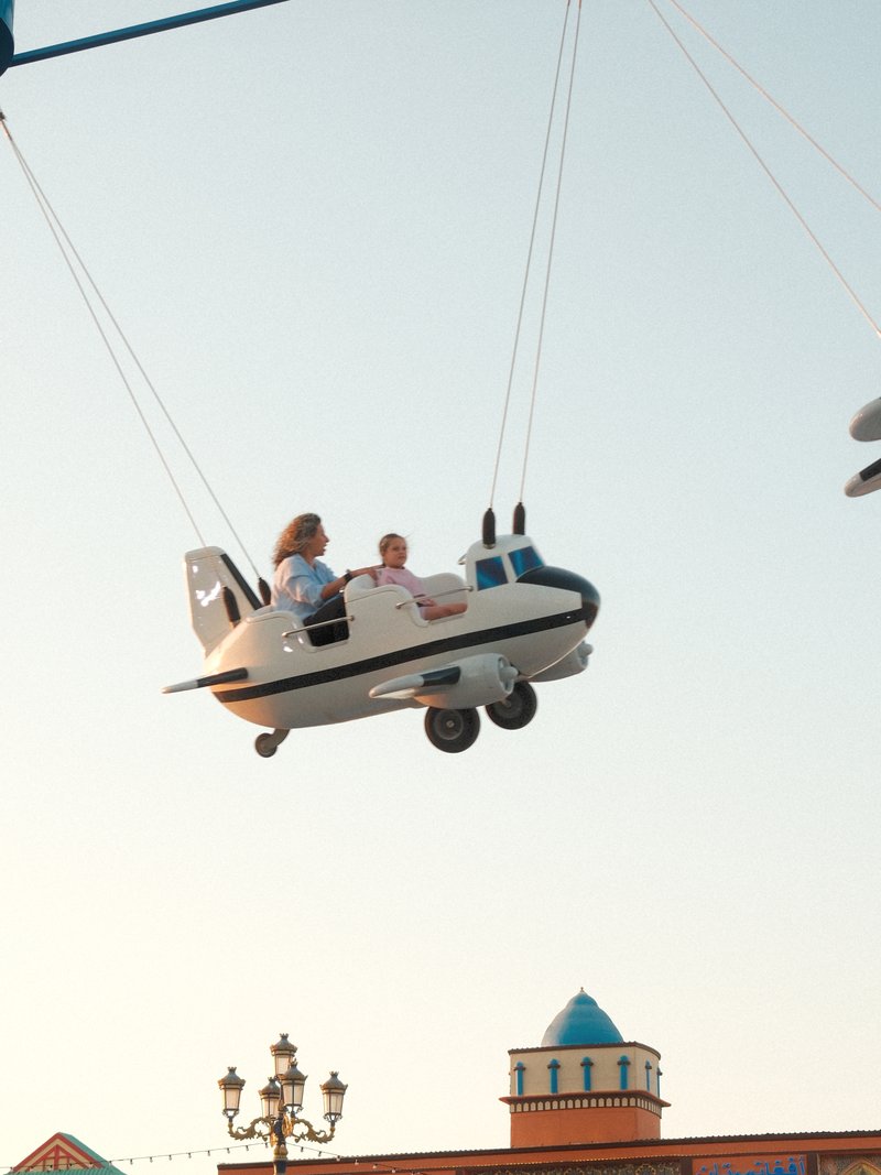 Two children enjoying a ride in a toy airplane suspended in the air against a clear sky.