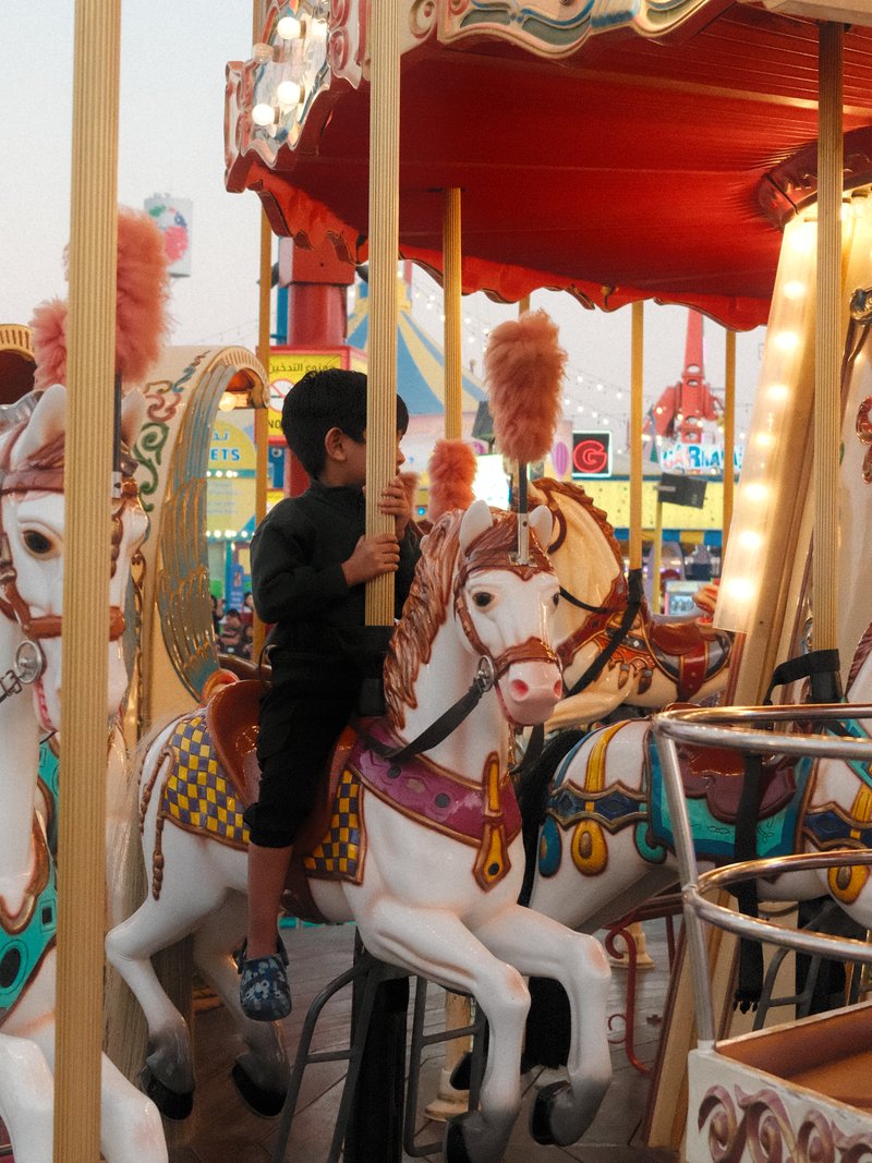 A child riding a carousel horse at a carnival, surrounded by colorful lights and decorations.