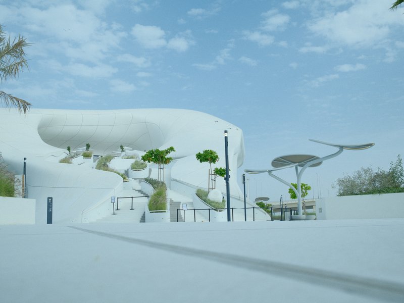 A modern architectural landscape with white structures, trees, and a clear blue sky.