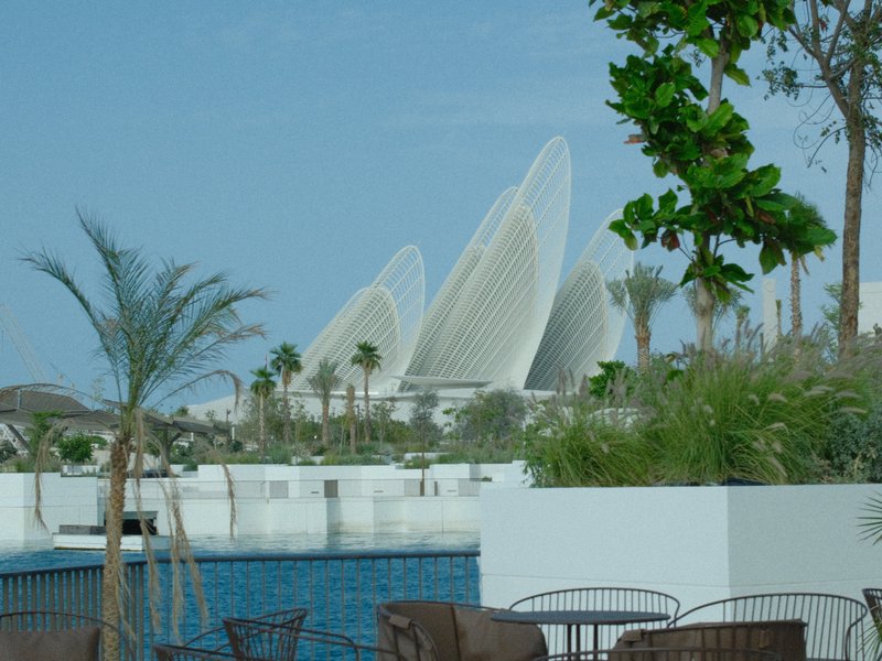 Modern architectural structure with curved white features against a clear blue sky, surrounded by greenery.